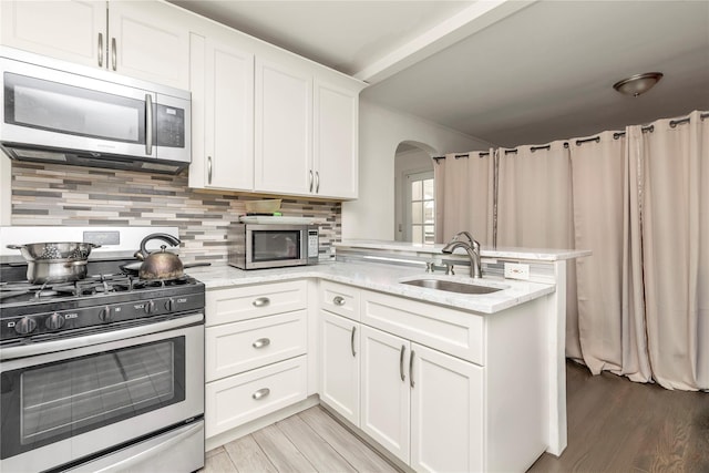 kitchen with a sink, stainless steel appliances, arched walkways, a peninsula, and backsplash