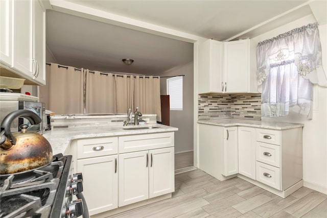 kitchen featuring white cabinets, light stone counters, decorative backsplash, and a sink