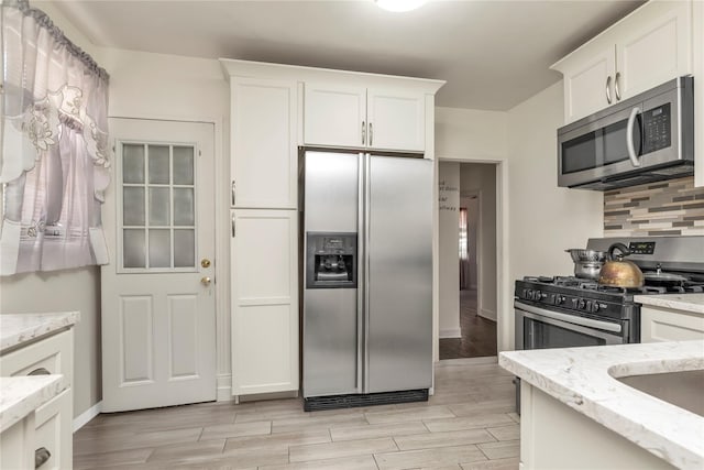 kitchen with backsplash, appliances with stainless steel finishes, light wood-style floors, and white cabinetry