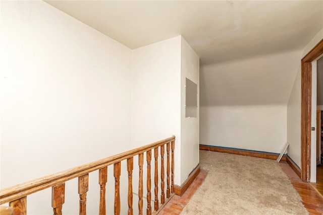 corridor featuring baseboards, wood finished floors, and electric panel