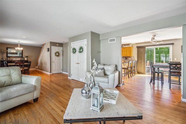 living room with baseboards, ceiling fan with notable chandelier, light wood-type flooring, and visible vents