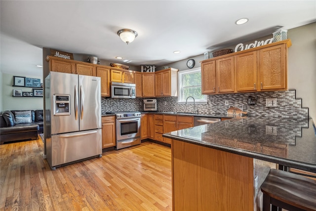 kitchen with a peninsula, a breakfast bar area, light wood-type flooring, a sink, and stainless steel appliances