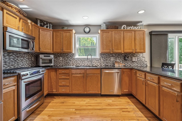 kitchen featuring stainless steel appliances, a sink, light wood-style flooring, and dark stone countertops