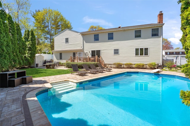 outdoor pool featuring fence, a deck, a shed, a patio area, and a diving board