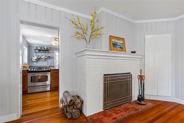 interior space with wood finished floors, a ceiling fan, crown molding, and a brick fireplace