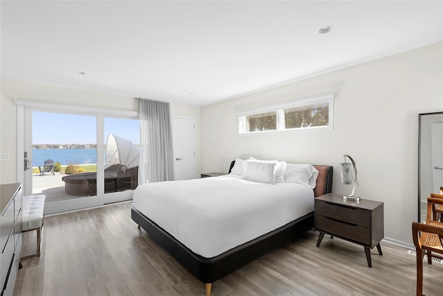 bedroom featuring light wood-style floors, access to exterior, and a water view