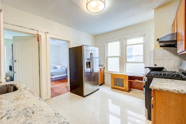 121-41 6th Ave, College Point, NY 11356 - kitchen featuring extractor fan, brown cabinetry, light tile patterned floors, appliances with stainless steel finishes, and light stone countertops