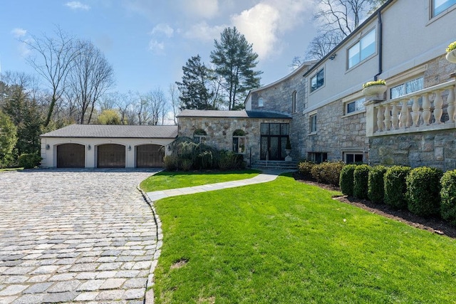 view of front of property featuring a front yard, driveway, stone siding, and a garage