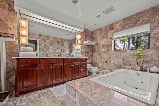 bathroom with tile walls, vanity, toilet, marble finish floor, and a tub with jets