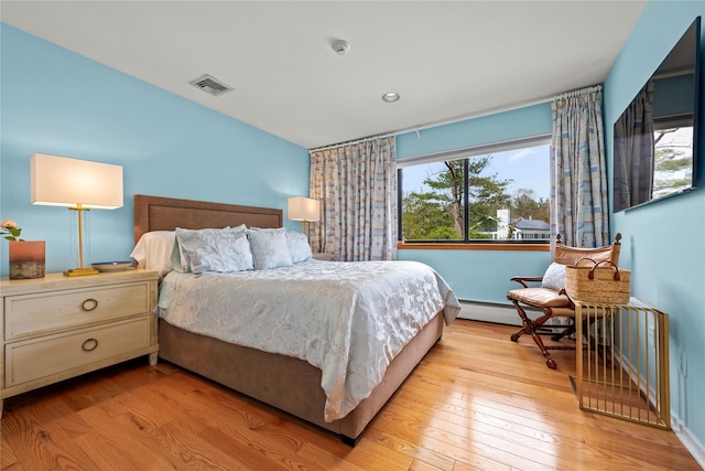 bedroom featuring baseboard heating, visible vents, multiple windows, and light wood-style flooring