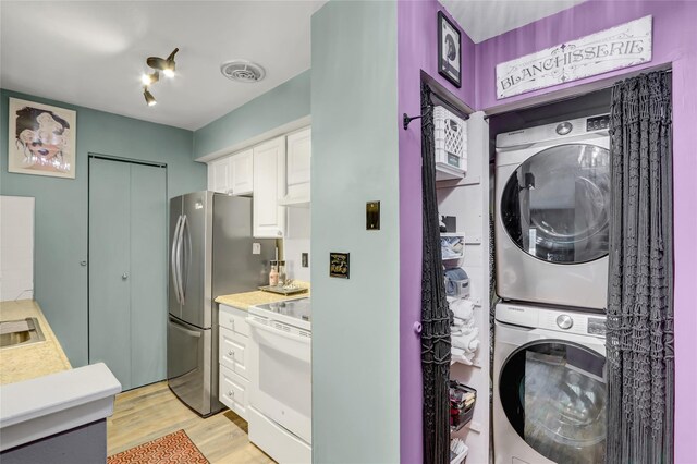 laundry room featuring light wood-type flooring, visible vents, stacked washing maching and dryer, and laundry area