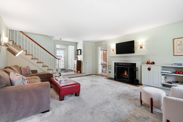 living room featuring a fireplace with flush hearth, carpet flooring, and stairs
