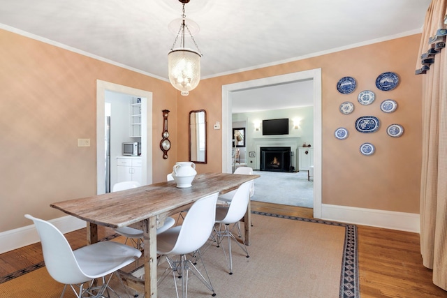 dining space with crown molding, baseboards, a lit fireplace, and wood finished floors