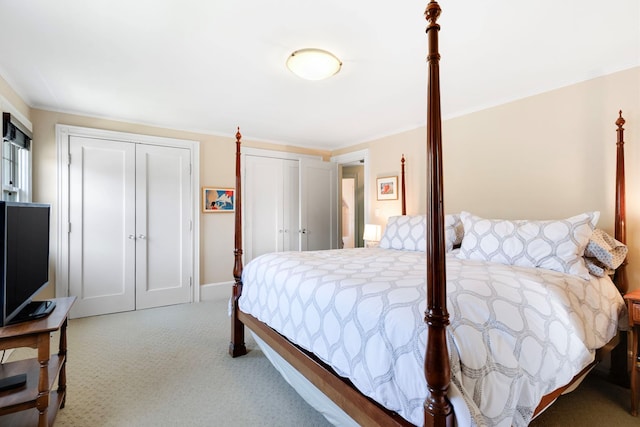 carpeted bedroom featuring baseboards, ornamental molding, and multiple closets