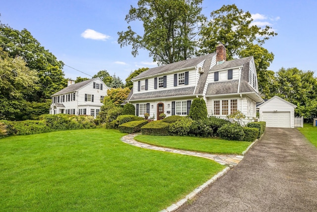 view of front of property with a chimney, a front yard, a garage, an outdoor structure, and aphalt driveway