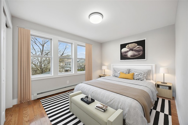 bedroom with wood finished floors and a baseboard heating unit