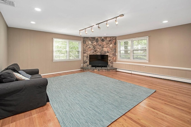 living room with visible vents, track lighting, wood finished floors, a fireplace, and a baseboard heating unit