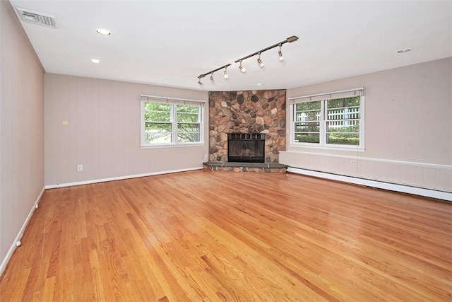 unfurnished living room featuring visible vents, wood finished floors, baseboards, a stone fireplace, and rail lighting