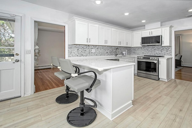 kitchen with a breakfast bar, light countertops, white cabinetry, a sink, and stainless steel appliances