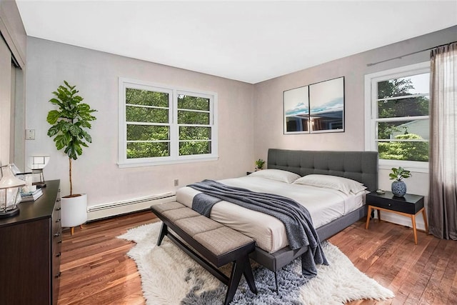 bedroom with a baseboard radiator, wood finished floors, and multiple windows
