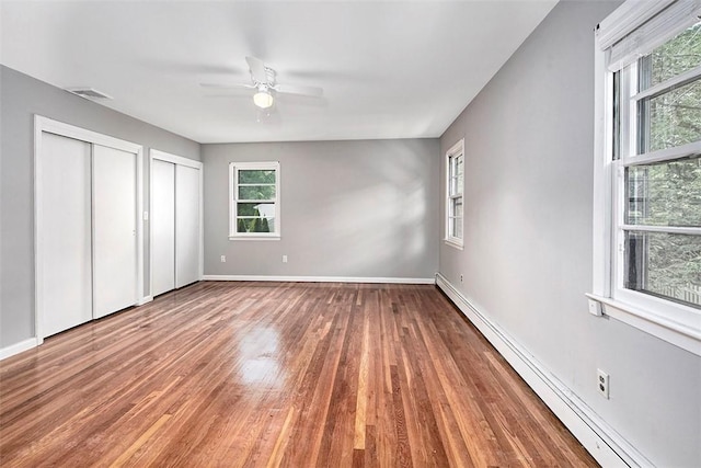 unfurnished bedroom featuring visible vents, two closets, baseboards, wood finished floors, and a baseboard heating unit