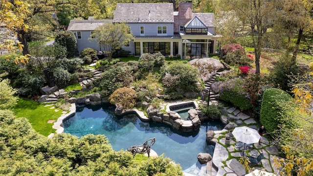 back of house featuring a chimney, an outdoor pool, a sunroom, a small pond, and a balcony
