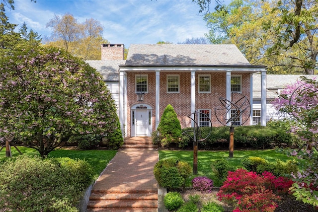 greek revival house featuring brick siding, an attached garage, and a chimney