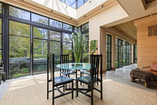 sunroom / solarium featuring a high ceiling, wooden ceiling, and stone tile flooring