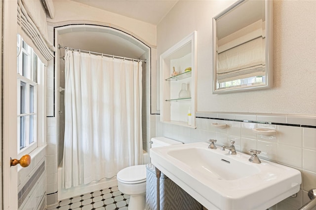 bathroom with a sink, tile walls, toilet, and shower / tub combo with curtain