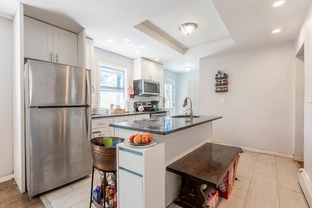 kitchen featuring white cabinets, a sink, a kitchen island with sink, dark stone counters, and stainless steel appliances
