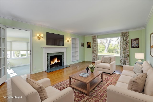living room with wood finished floors, crown molding, a high end fireplace, and built in shelves