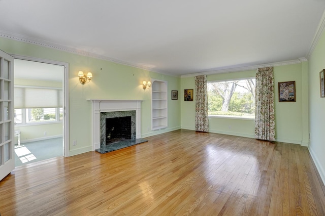 unfurnished living room with a high end fireplace, light wood-style floors, crown molding, and built in features