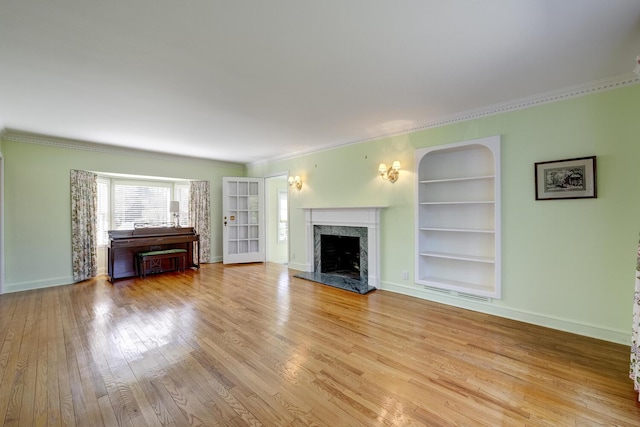 unfurnished living room featuring built in shelves, a premium fireplace, baseboards, and light wood-type flooring