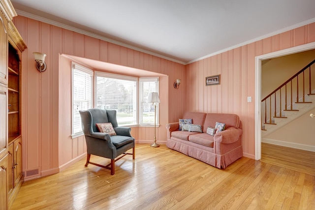 living area with stairs, light wood-style flooring, baseboards, visible vents, and crown molding