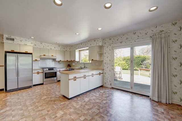 kitchen with wallpapered walls, stainless steel appliances, a sink, visible vents, and a peninsula