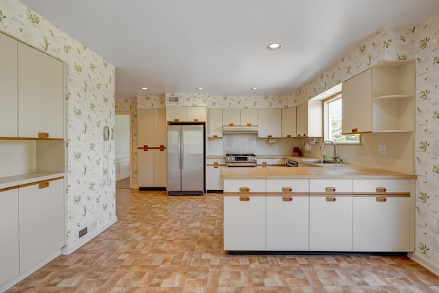 kitchen with open shelves, a sink, appliances with stainless steel finishes, wallpapered walls, and a peninsula