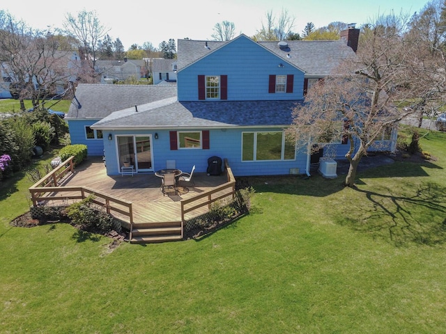 rear view of property featuring a lawn, a chimney, a deck, and a shingled roof