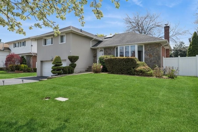 tri-level home with an attached garage, fence, a chimney, and a front lawn