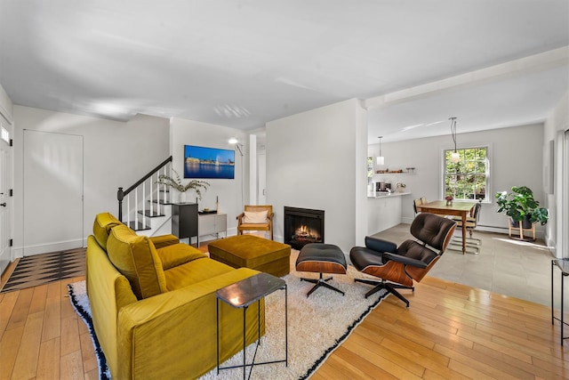 living room featuring wood-type flooring, a warm lit fireplace, and stairway