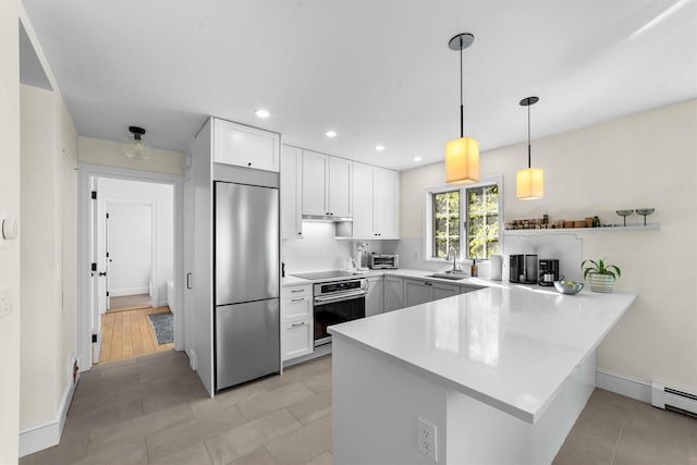 kitchen with white cabinets, appliances with stainless steel finishes, a sink, light countertops, and a peninsula