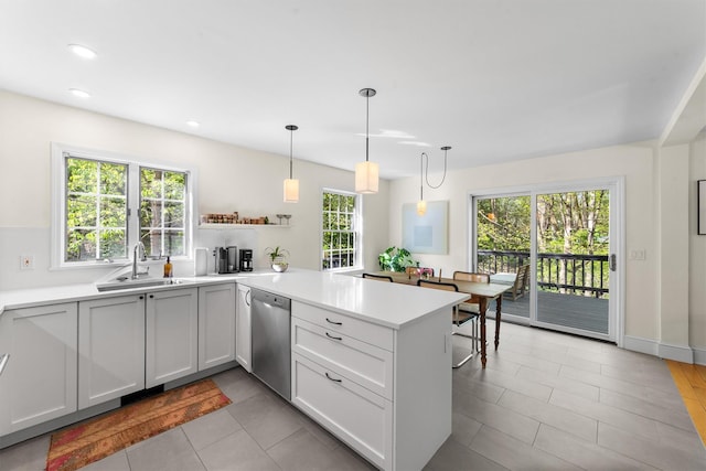 kitchen featuring stainless steel dishwasher, a sink, a peninsula, and light countertops