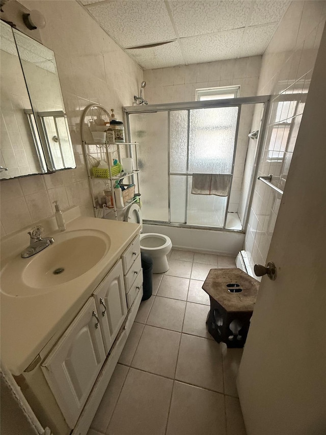 full bath featuring shower / bath combination with glass door, toilet, tile walls, tile patterned flooring, and vanity