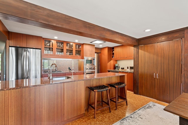 kitchen featuring a sink, light stone counters, glass insert cabinets, and appliances with stainless steel finishes