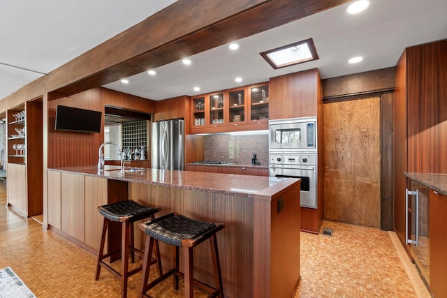 kitchen featuring appliances with stainless steel finishes, modern cabinets, a kitchen breakfast bar, and brown cabinetry