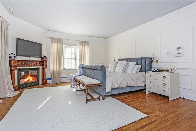 bedroom featuring a glass covered fireplace, ornamental molding, a decorative wall, and wood finished floors