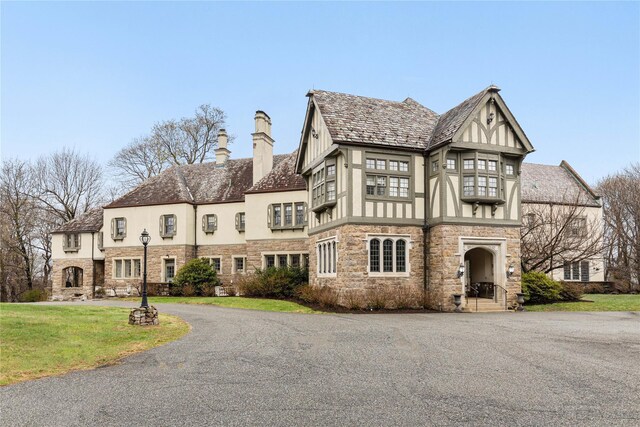 exterior space featuring a front yard, a chimney, stone siding, and stucco siding
