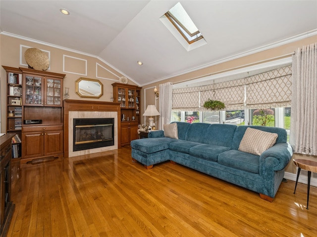 living area featuring vaulted ceiling with skylight, wood-type flooring, a tiled fireplace, and ornamental molding