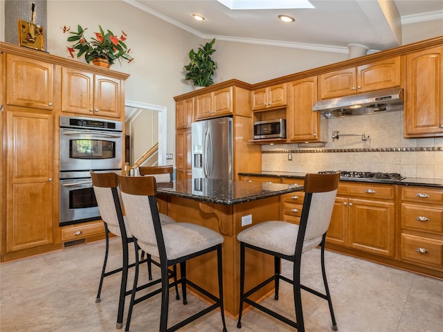 kitchen featuring a breakfast bar area, under cabinet range hood, decorative backsplash, a kitchen island, and appliances with stainless steel finishes