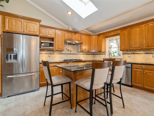 kitchen featuring under cabinet range hood, a kitchen bar, appliances with stainless steel finishes, and lofted ceiling with skylight