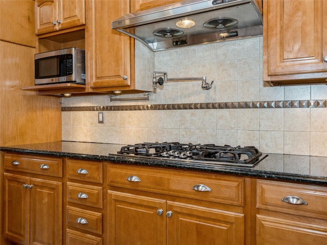 kitchen with extractor fan, stainless steel appliances, dark stone counters, brown cabinets, and decorative backsplash